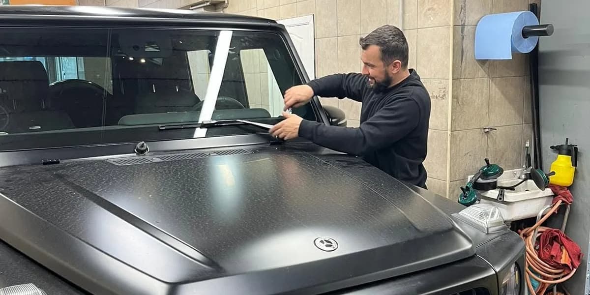 Monteur van Autoglas Perfect werkt aan de voorruit van een matzwarte Mercedes G-klasse in de werkplaats