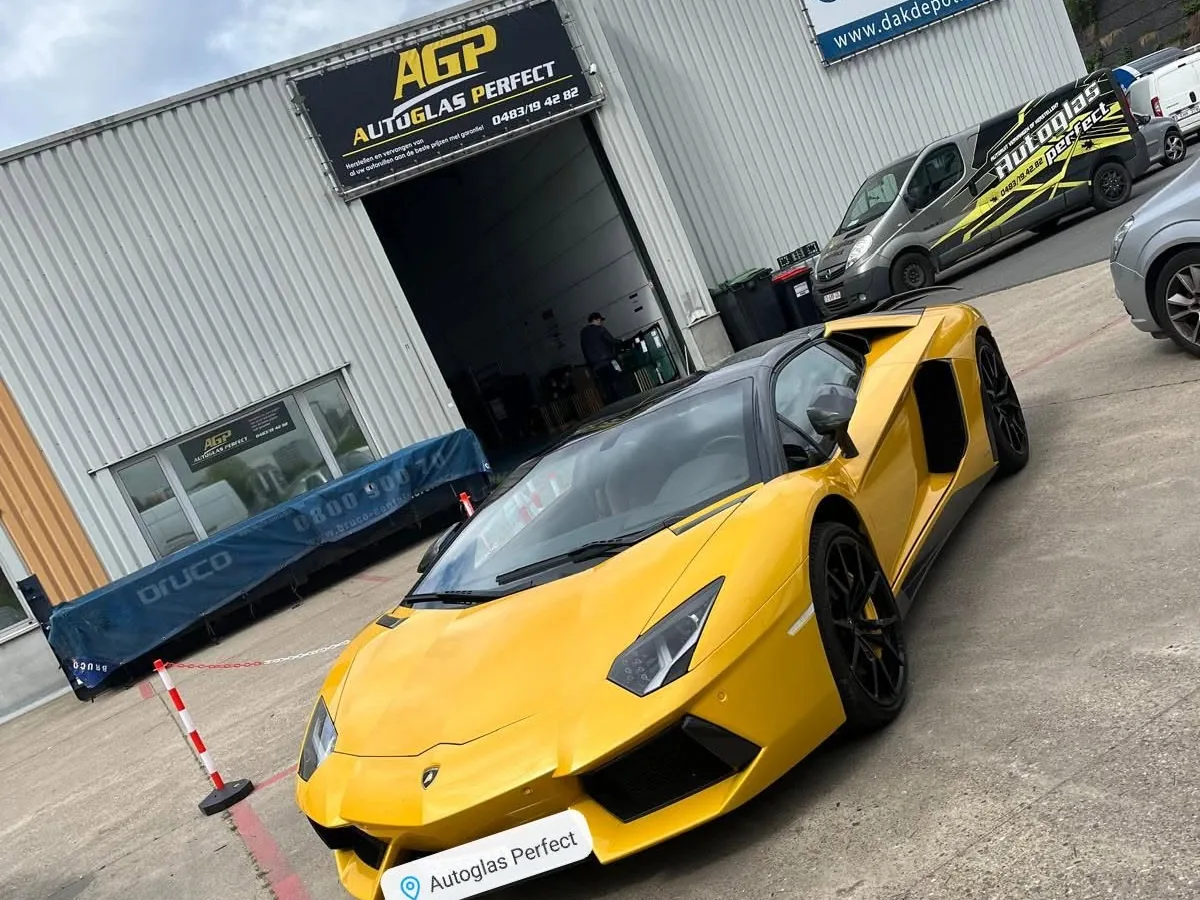 Een gele Lamborghini voor de werkplaats van Autoglas Perfect, onder het zwart-gele spandoek